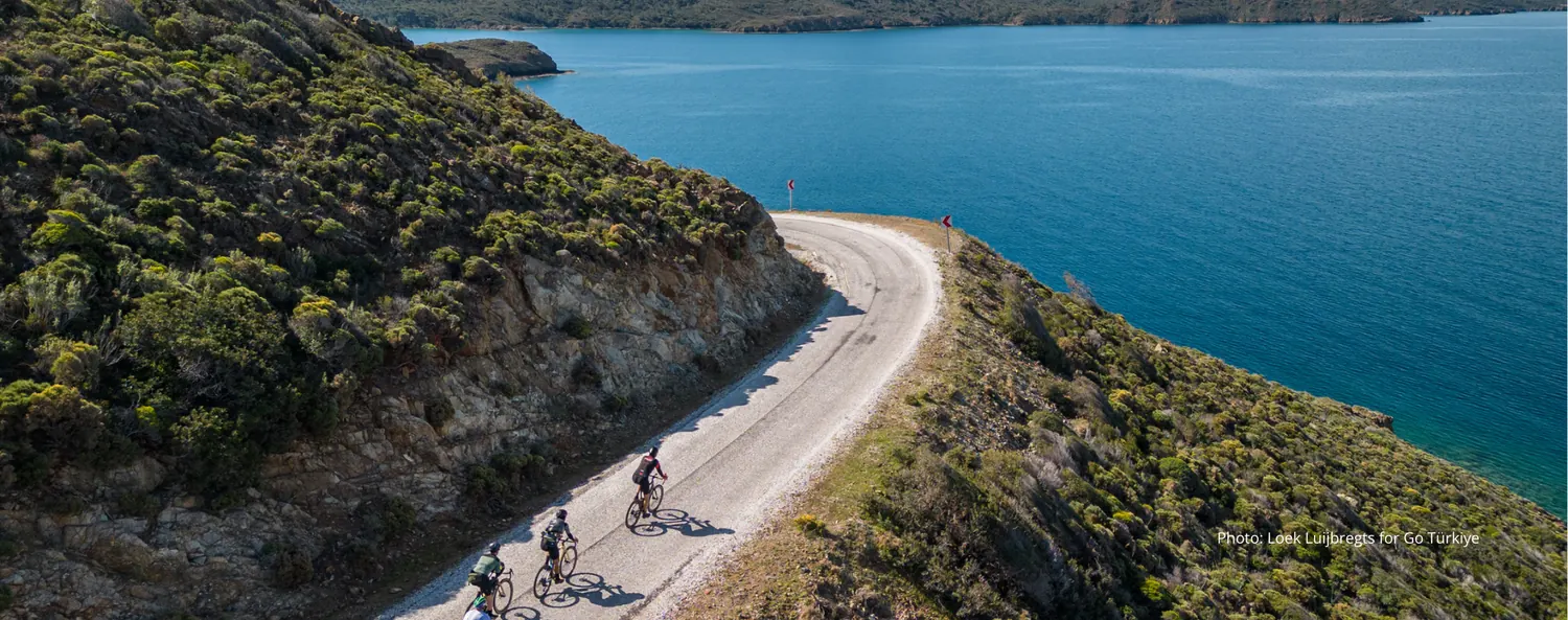 Cyclists on a gravel road along the turquoise coastline of the Marmaris peninsula, Türkiye