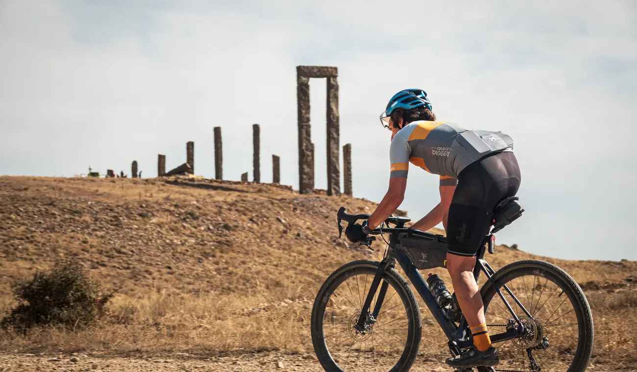 A bikepacker climbing a gravel road towards standing stone ruins